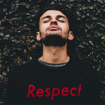 Foto: Junger Mann lehnt sich mit geschlossenen Augen an begrünte Mauer und trägt einen Pulli mit "Respect"-Aufschrift